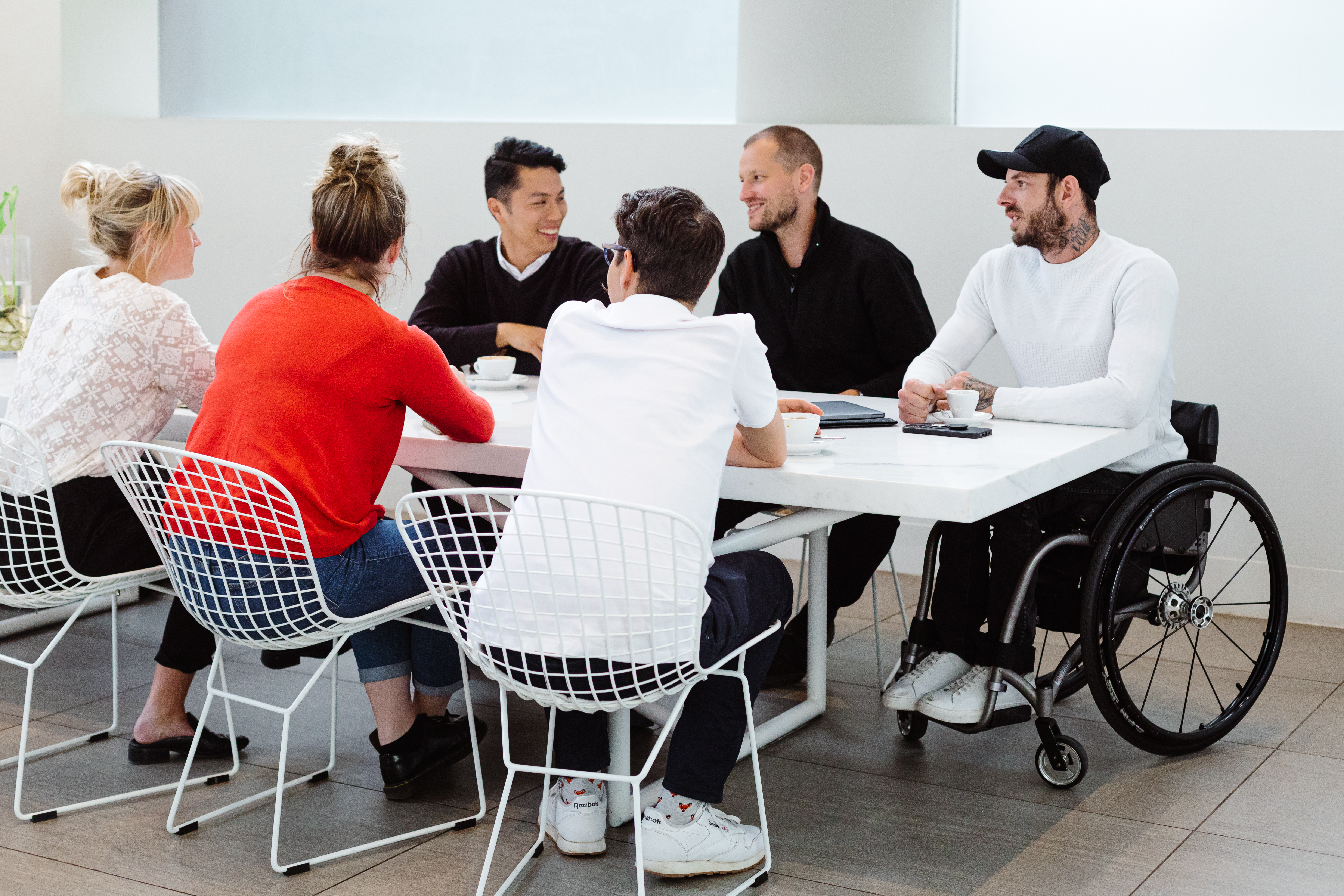 6 people sitting around a table looking at each other and smiling/laughing