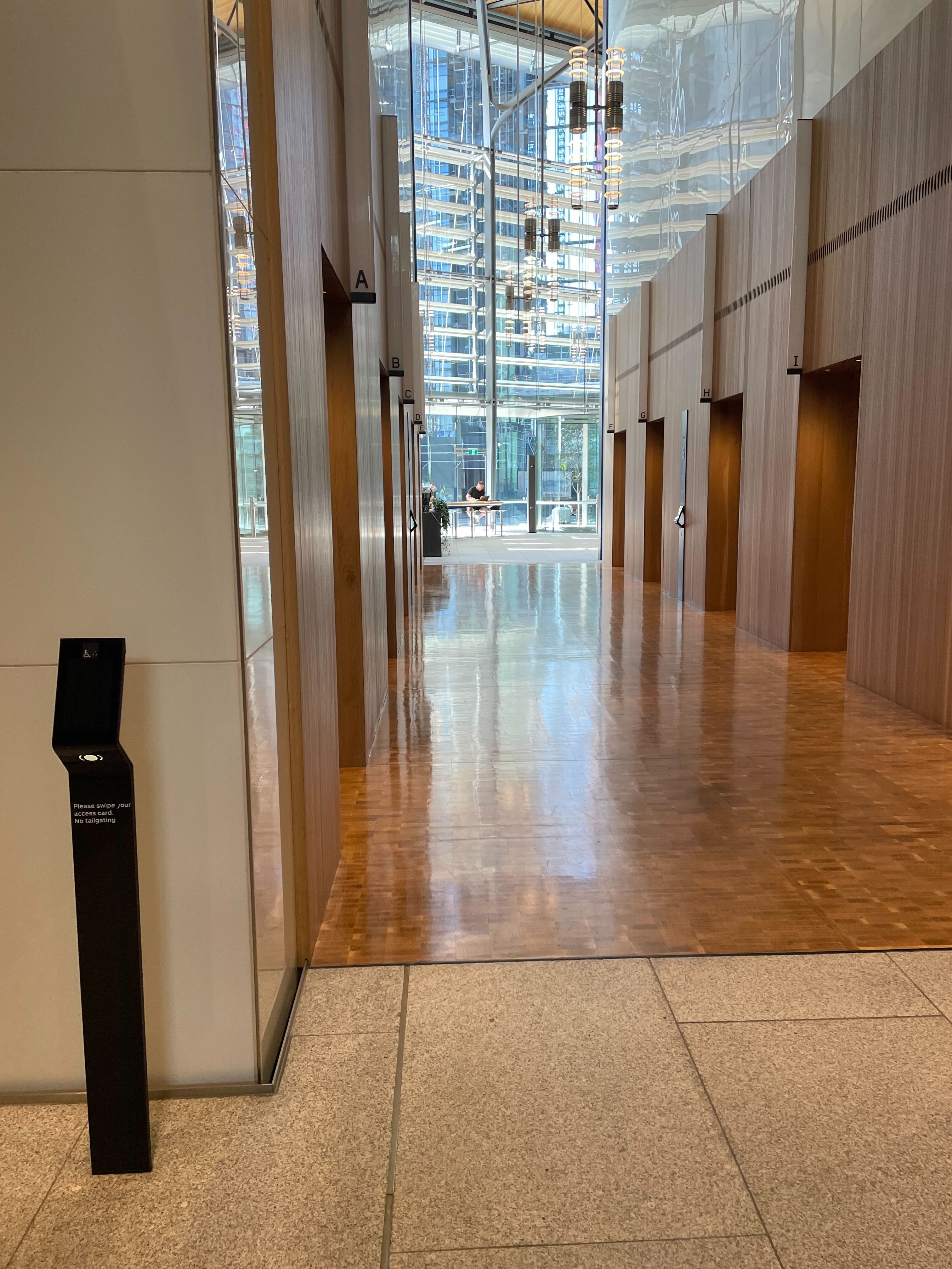 Image of lifts at lobby level with swipe card entry. The flooring and walls are paneled with wood. 
