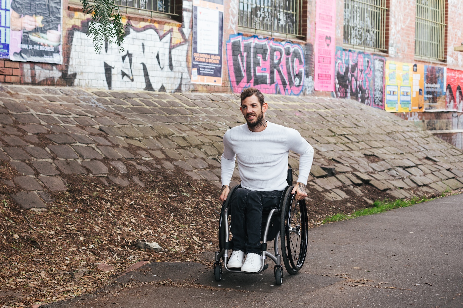 A man who is a wheelchair user is wheeling himself through a colourful laneway. 