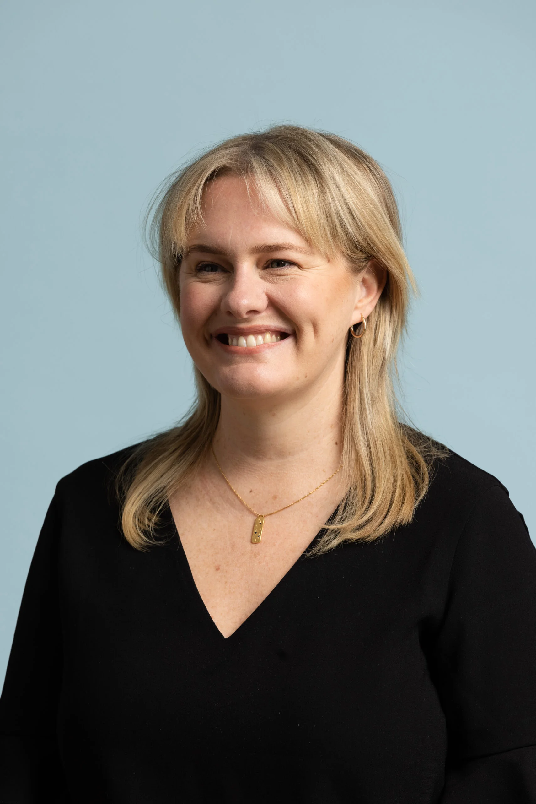 A close-up image of Melissa, a Caucasian woman with blonde hair. She is smiling and looking away from the camera, wearing a black shirt.