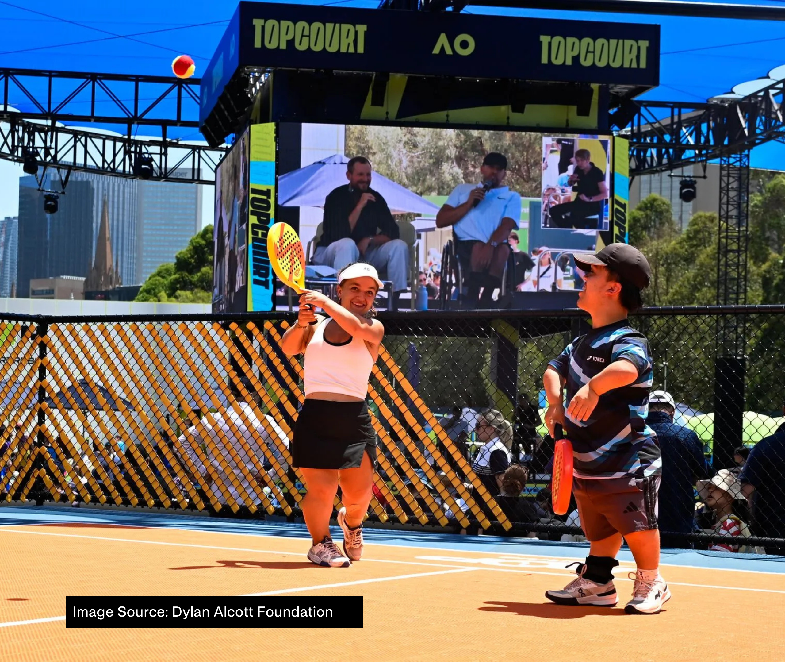 At AO 2025, a large screen shows Dylan Alcott and Zack Alcott speaking with an Auslan interpreter beside them under the heading "Top Court". In the foreground, two short statured tennis players are playing on court.
