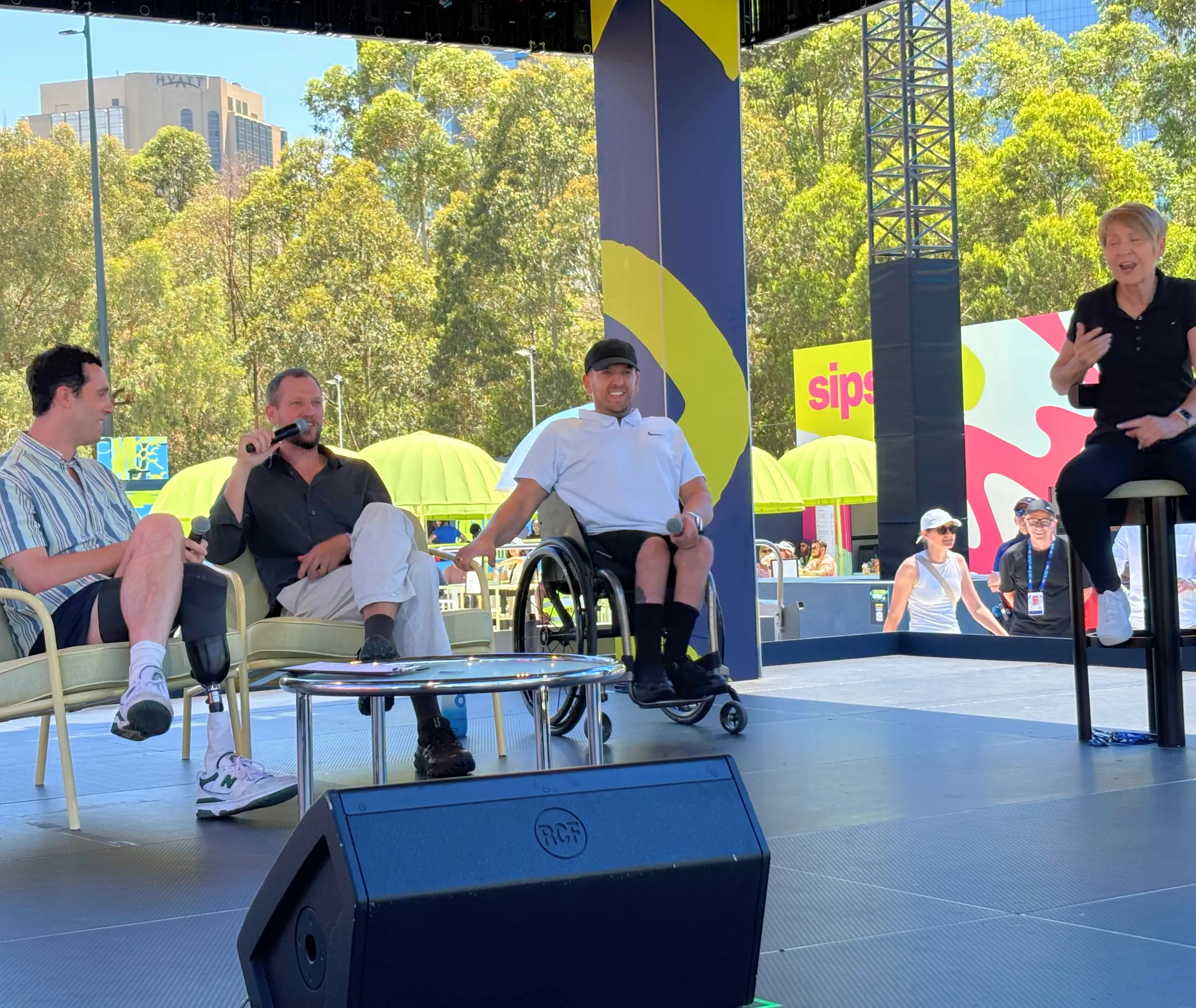 Dylan Alcott and Zack Alcott on the Top Court stage at AO 2025, standing beside an Auslan interpreter and the host of the chat.