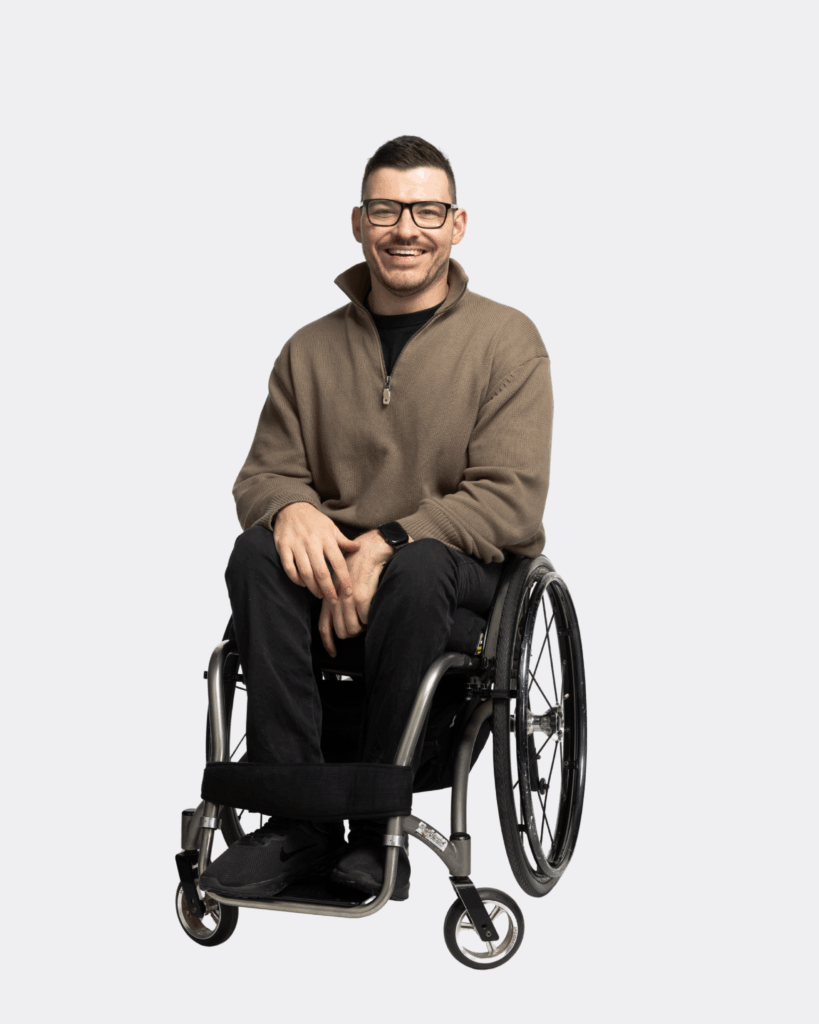 Oliver Hunter, a wheelchair user is wearing black trousers and brown shirt, looking at the camera and smiling.