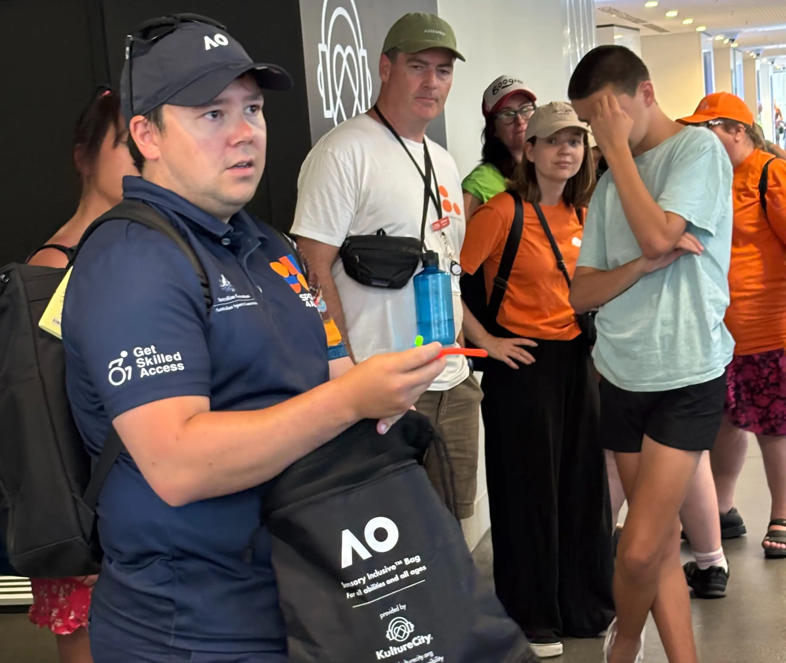 Sport4All Inclusion Coach Oliver, wearing a Sport4All polo and seated in a wheelchair, speaks to a group gathered in a circle around him.