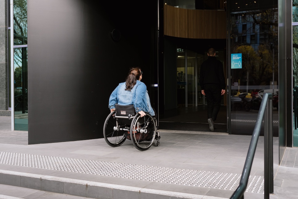 A woman who is a wheelchair user is entering an office building.