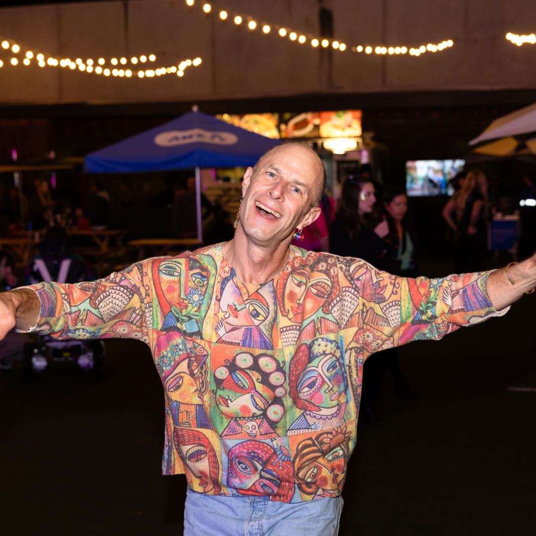 Person smiling with arms outstretched at an event.