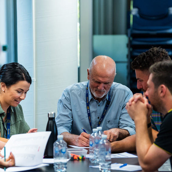 A group of people sit at a table, working together in a learning environment.